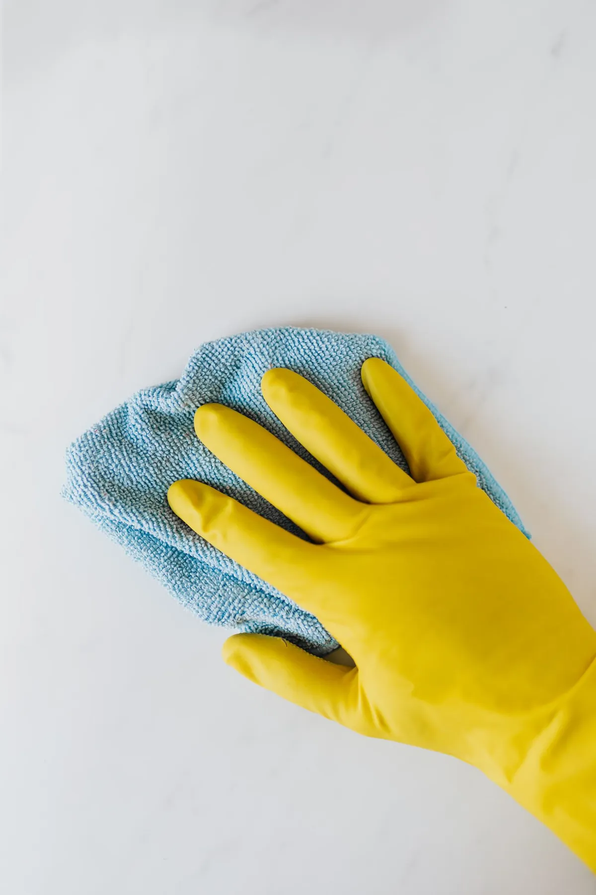 Hand im gelben Handschuh wischt eine Oberfläche mit einem Mikrofasertuch